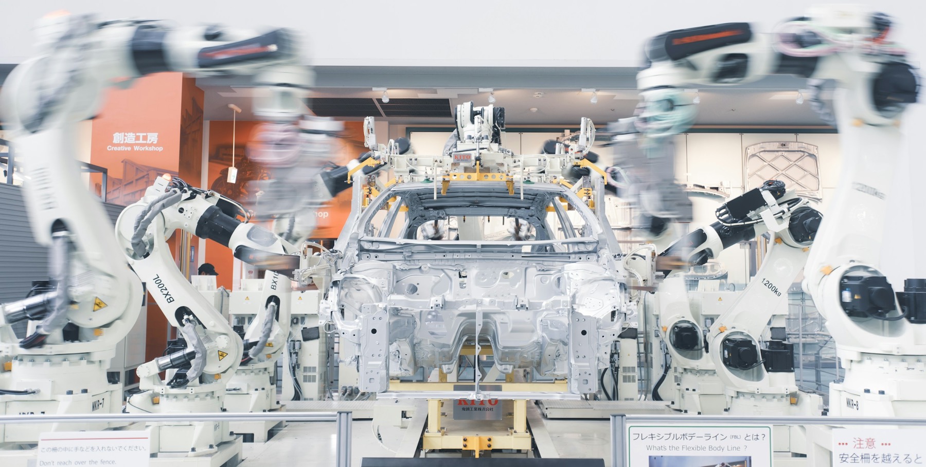 White industrial robots around a car body behind a safety fence