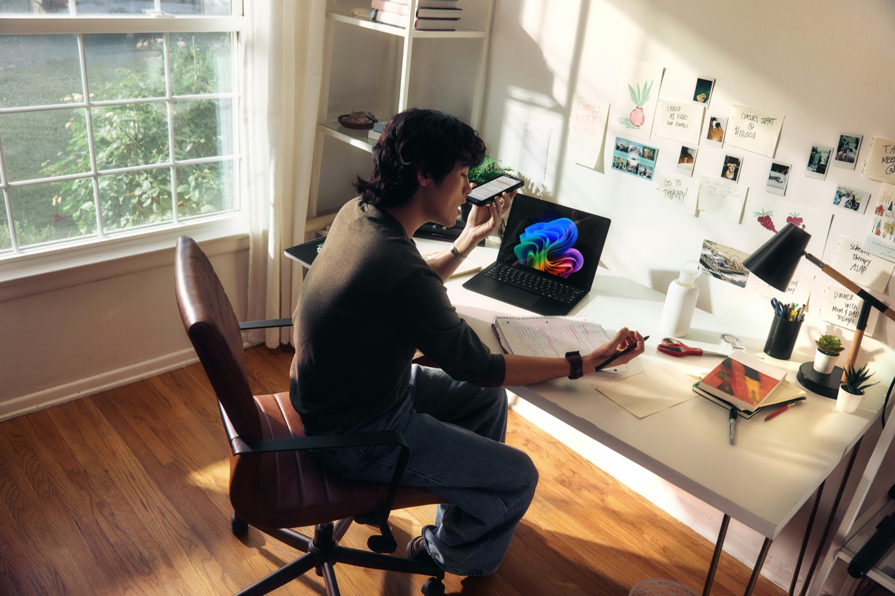 A person working at a home office desk with a laptop, phone and notebook