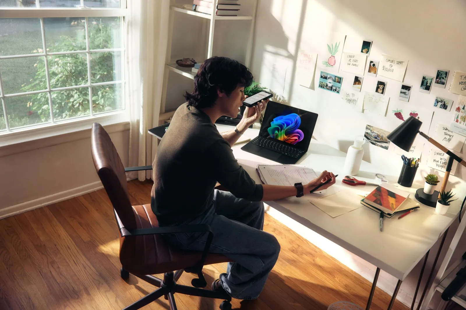 A person working at a home office desk with a laptop, phone and notebook